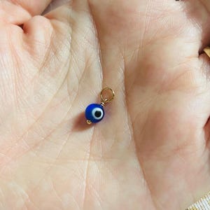 May include: A small gold charm featuring a blue evil eye bead. The charm is ideal for adding a touch of protection and good luck to any piece of jewellery.