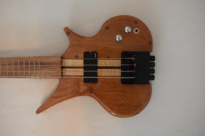May include: A wooden electric bass guitar with a unique body shape and a black pickup. The guitar has a natural wood finish and a black bridge.