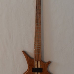 May include: A wooden bass guitar with a unique body shape and a natural wood finish. The guitar has a black pickguard and black tuning pegs.