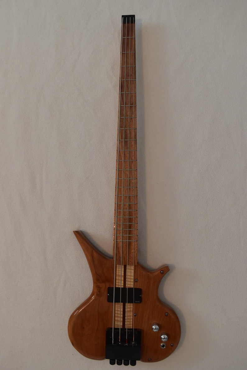 May include: A wooden bass guitar with a unique body shape and a natural wood finish. The guitar has a black pickguard and black tuning pegs.