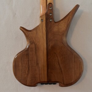 May include: A wooden electric bass guitar with a unique body shape and a light brown finish. The body is made of two pieces of wood, with a dark brown stripe down the center.