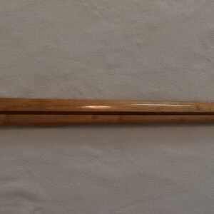 May include: A close-up of a wooden guitar neck with a natural finish. The neck has a dark wood inlay running down the center.