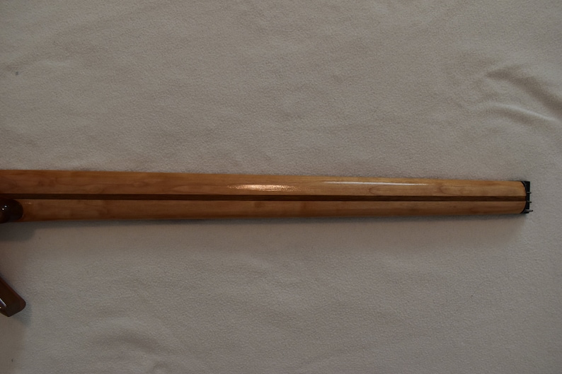 May include: A close-up of a wooden guitar neck with a natural finish. The neck has a dark wood inlay running down the center.