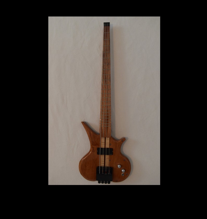 May include: A brown wooden bass guitar with a unique body shape and a black pickguard. The guitar has a single pickup and a set of tuning keys.
