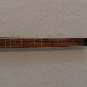 May include: Close-up of the fretboard of a wooden bass guitar. The fretboard is made of a light brown wood with silver frets.
