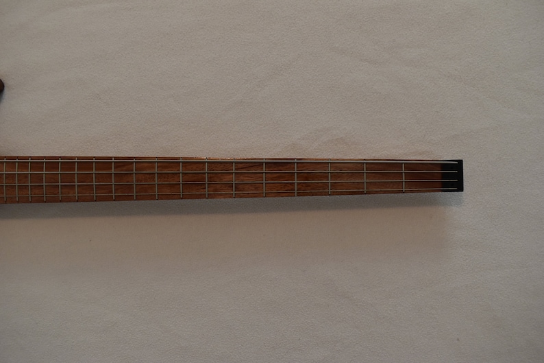 May include: Close-up of the fretboard of a wooden bass guitar. The fretboard is made of a light brown wood with silver frets.