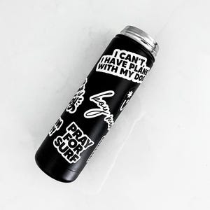 A black insulated water bottle with various stickers on it, including one that says "I CAN'T I HAVE PLAN WITH MY DOG".
