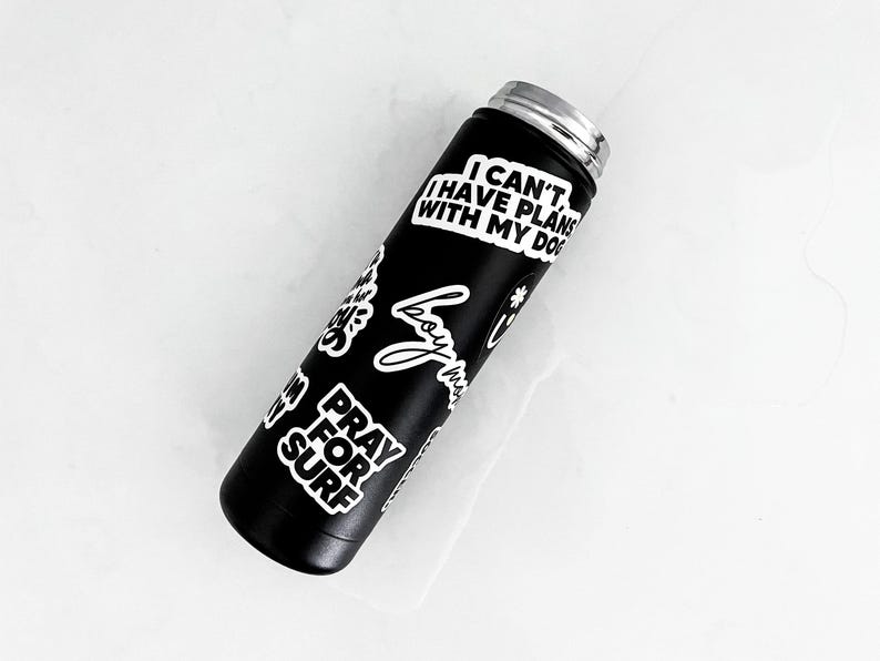 A black insulated water bottle with various stickers on it, including one that says "I CAN'T I HAVE PLAN WITH MY DOG".