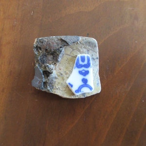 May include: A close-up of a blue and white ceramic shard with a floral design. The shard is sitting on a piece of broken pottery.