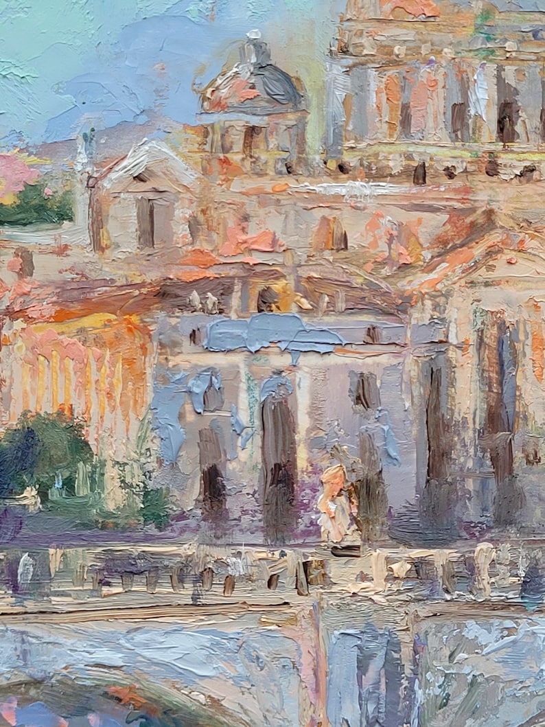 May include: Oil painting of a European cityscape with buildings in shades of beige, orange, and gray. The artwork features a dome and architectural details, with a light blue sky in the background. The brushstrokes are visible, creating a textured effect.