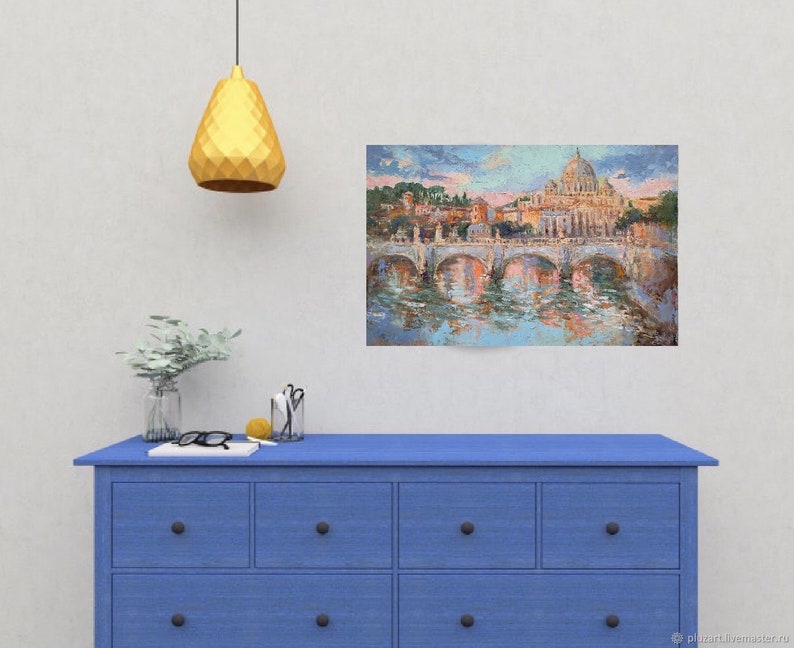 May include: An oil painting depicting a cityscape with a bridge and a large domed building, likely a cathedral. The artwork is displayed on a wall above a blue dresser. The painting's colors include blues, oranges, and greens, reflecting in the water.