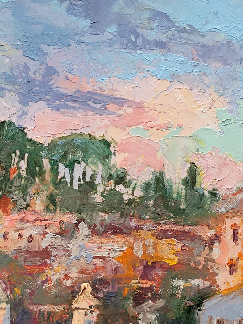 May include: Impasto oil painting of a cityscape at sunset. The sky is a blend of pink, blue, and lavender hues, with textured brushstrokes. Buildings with orange and brown roofs are visible below green trees. The artwork evokes a sense of warmth and tranquility.