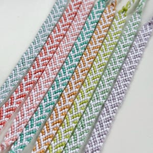 May include: Close-up of several handmade friendship bracelets in various colors, including light blue, coral, teal, yellow, and lavender. Each bracelet features a chevron pattern in white, creating a textured and colorful accessory.