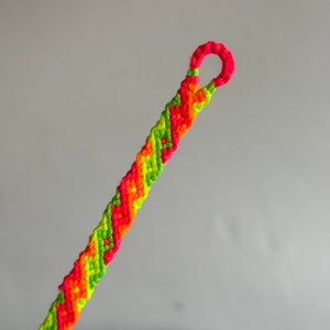 May include: A friendship bracelet with a green, orange, and pink chevron pattern.
