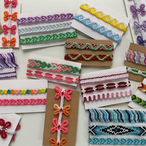 May include: Assortment of colourful friendship bracelets with various patterns and designs. The bracelets are displayed on white and brown card stock.