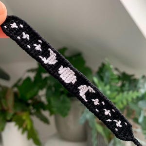 Könnte beinhalten: Schwarzes Freundschaftsarmband mit weißen, gewebten Mond- und Sternmotiven.