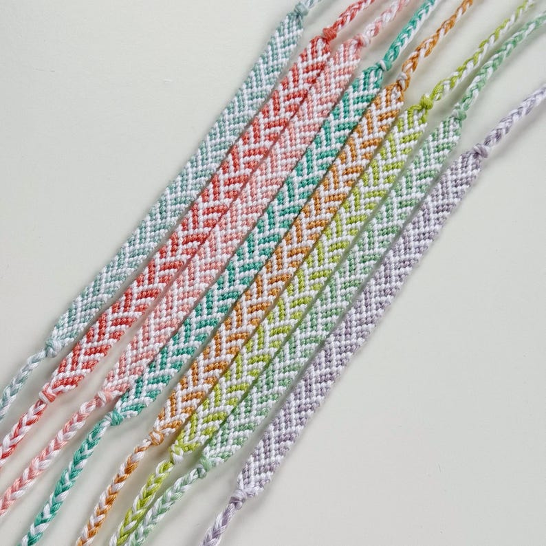 May include: A collection of colorful friendship bracelets. Each bracelet features a chevron pattern in a different color, including red, teal, orange, green, and purple. The bracelets are made of woven thread.
