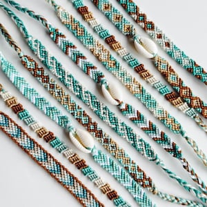 May include: A set of seven colourful friendship bracelets with a white seashell charm on each. The bracelets are made with a variety of colours, including turquoise, brown, white, and beige. The bracelets are woven in a chevron pattern.