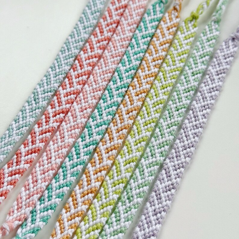 May include: Close-up of several colorful friendship bracelets. Each bracelet features a chevron pattern in various colors, including pink, teal, orange, yellow, and purple. The bracelets are made of woven thread.