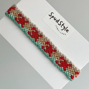May include: A red, beige and teal friendship bracelet with a woven pattern. The bracelet is on a white card with the text "SpudStyle Jewellery".