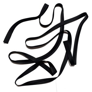 May include: A long, continuous strip of black bias tape folded into a narrow, flat band. The fabric ribbon is arranged in loose, overlapping loops and curves, showcasing its smooth, matte texture and consistent width throughout the entire length.