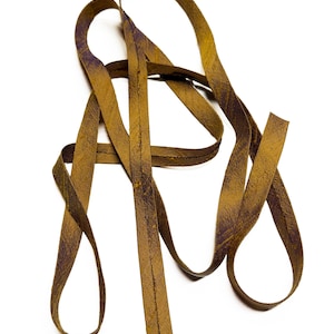 May include: A close-up shot of a length of brown leather ribbon, with a textured surface and a slight purple hue in some areas. The ribbon is looped and curved against a white background.