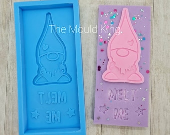 May include: A blue silicone mould with a pink gnome design. The gnome is wearing a red hat and has a white beard. The mould says "Melt Me" in white letters.