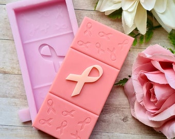 May include: Pink silicone mold for making a pink ribbon-shaped candle. The mold has a large pink ribbon in the center and smaller pink ribbons around the edges.