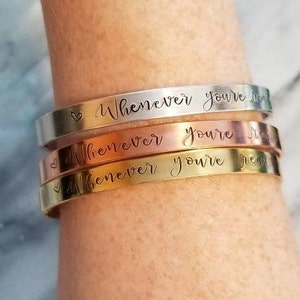 May include: Three stacked bracelets with the inscription "Whenever you're near" on each. The bracelets are silver, rose gold, and gold.