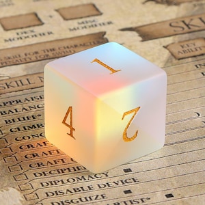 May include: A translucent, square-shaped die with gold-colored numbers 1, 2, and 4 visible. The die has a rainbow-like effect on its surface. The background features a character sheet with text including "SKILL" and "DEX MODIFIER".