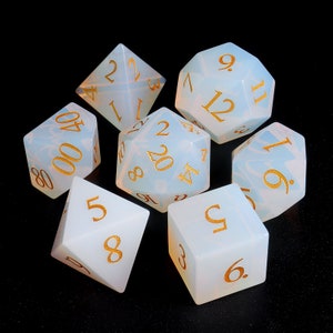 May include: Set of seven white opaque dice with gold numbers. The dice are a d4, d6, d8, d10, d%, d12, and d20.
