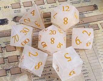 May include: A set of eight white dice with gold numbers. The dice are on a table with a game board in the background.
