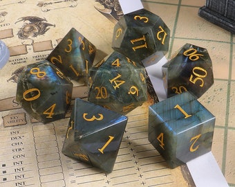 May include: Set of six green and gold gemstone dice with numbers 1 through 6. The dice are on a brown and white surface with a grid pattern.
