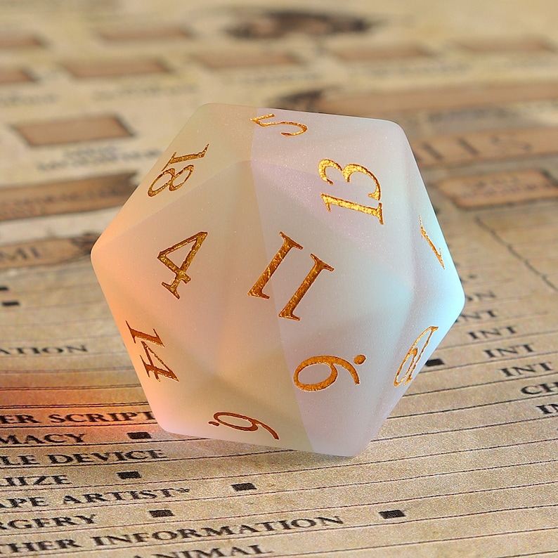 May include: A frosted, off-white twenty-sided die with gold-colored numerals. The die is resting on a vintage-style paper background. The numbers are clearly visible, and the die appears to be made of a translucent material.