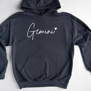 May include: A dark gray hooded sweatshirt with the word "Gemini" written in white cursive with a small white heart next to it.