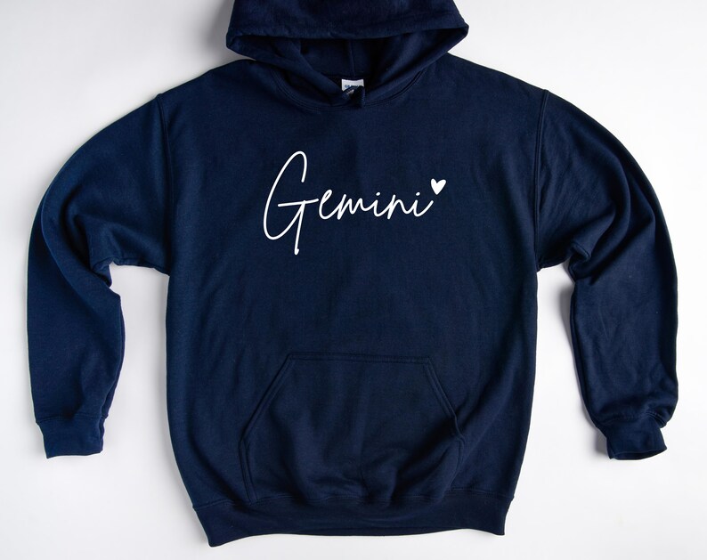May include: A navy blue hoodie with a white cursive inscription that reads "Gemini" with a small white heart to the right of the word.