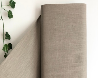 May include: A roll of light brown fabric with a subtle textured weave. The fabric is folded in half and the edges are visible.