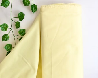 May include: A pale yellow fabric with a slightly rough texture. The fabric is folded and draped on a white surface.