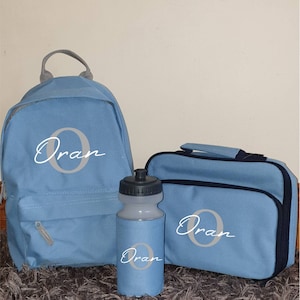 以下が含まれることがあります： 青いバックパック、ランチバッグ、水筒に「Oran」という名前が白い文字で書かれており、文字「O」の周りに灰色の円があります。