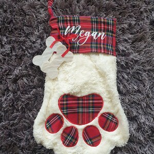 Op de afbeelding: Witte pluche kerstsok met een rood en zwart ruitpatroon met een pootprint. De sok heeft een rood en zwart ruitpatroon met de naam "Megan" geborduurd in wit.