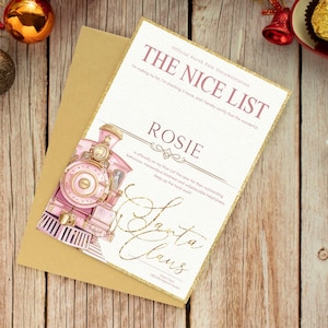 May include: A rectangular card with a gold glitter border featuring a pink steam locomotive illustration and the text THE NICE LIST, ROSIE, and Santa Claus in a cursive font, resting on a tan envelope with a white background and grid pattern.