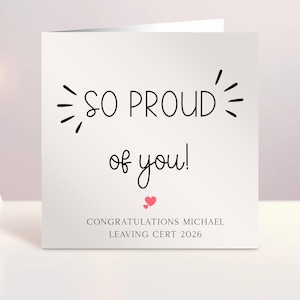 Może przedstawiać: Kwadratowa biała kartka okolicznościowa z czarnym napisem SO PROUD of you! oraz małymi czarnymi liniami dekoracyjnymi po bokach. Poniżej tekstu znajdują się dwa małe różowe serduszka oraz napis CONGRATULATIONS MICHAEL LEAVING CERT 2026.