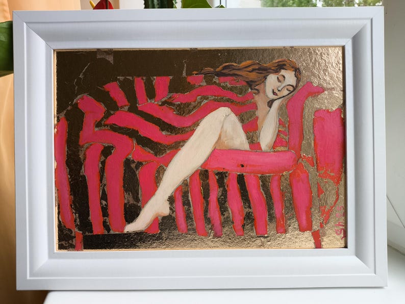 Pode incluir: Pintura emoldurada que retrata uma figura reclinada numa chaise longue &agrave;s riscas rosa e pretas. A obra de arte apresenta um fundo dourado e uma moldura branca. A figura tem cabelo comprido castanho e est&aacute; pintada numa pose relaxada.