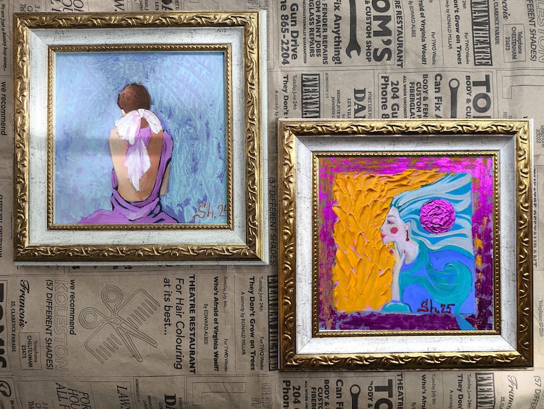 Pode incluir: Duas pinturas emolduradas com molduras douradas e brancas ornamentadas. A pintura da esquerda retrata uma figura em um vestido roxo com um len&ccedil;o branco. A pintura da direita mostra uma mulher com cabelo amarelo e rosto azul. Ambas as pinturas s&atilde;o assinadas.