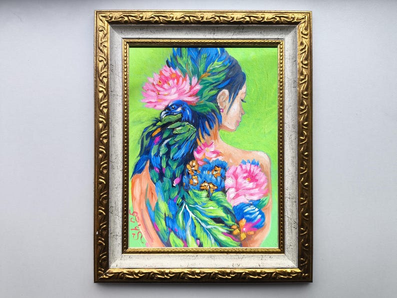 Pode incluir: Obra de arte emoldurada com as costas de uma mulher adornadas com um pav&atilde;o e desenhos florais. A pintura apresenta cores vibrantes, incluindo azul, verde, rosa e laranja, sobre um fundo verde. A moldura &eacute; dourada com uma borda interna branca.