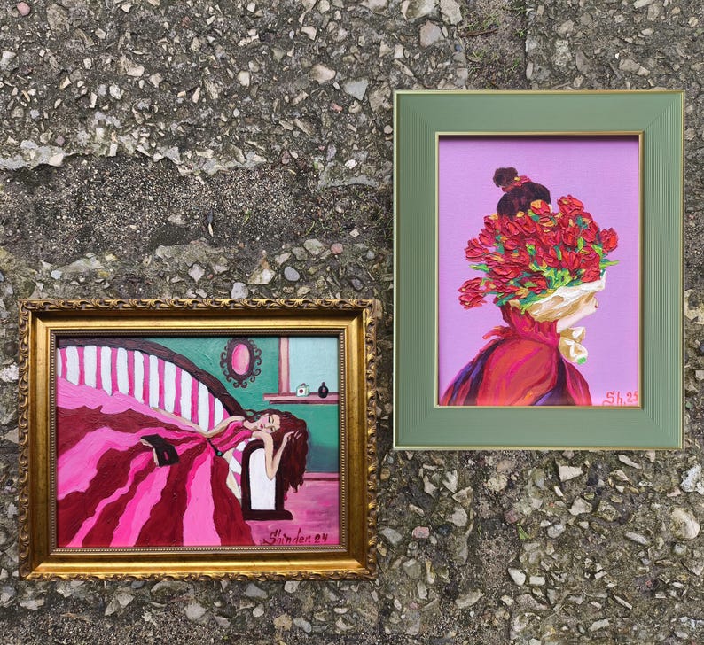 Pode incluir: Duas pinturas emolduradas. Uma apresenta uma mulher com um vestido rosa reclinada em uma cama listrada. A outra retrata uma figura com uma cabe&ccedil;a de flores vermelhas em um fundo roxo. Ambas s&atilde;o exibidas em uma superf&iacute;cie cinza texturizada.