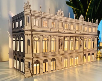 May include: A detailed paper model of a large, ornate building with multiple windows and a symmetrical design. The model is lit from within, creating a warm glow.