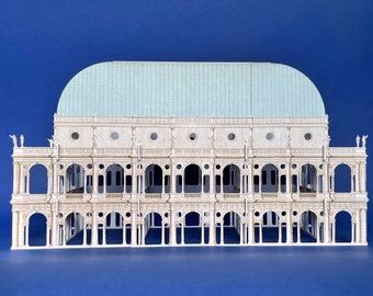 May include: A white paper model of a building with a light blue roof. The building has many arches and columns. The model is on a blue background.