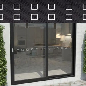 May include: A black framed sliding glass door with a view of a kitchen interior. The door is flanked by green leafy plants in pots. The door has a series of small square white stickers along the bottom edge.