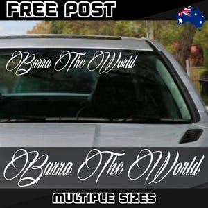 May include: A silver car with a white windscreen sticker displaying the words "Barra The World" in a cursive font. The text "MULTIPLE SIZES" is at the bottom. The words "FREE POST" are at the top.